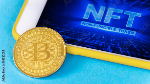 Physical Bitcoin gold coin and smartphone with NFT in it, blue background photo