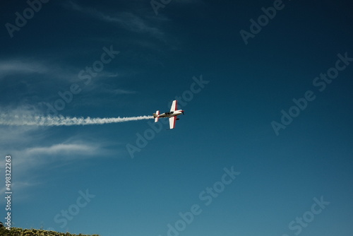  A small plane maneuvers in a blue sky with a contrail. High quality photo