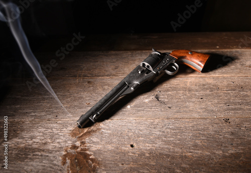 Fotografi smoke streams from the barrel of an old gun laying on saloon floor