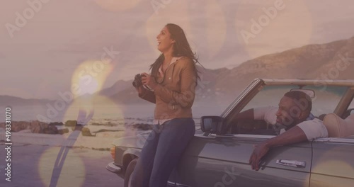 Animation of light spots over happy diverse couple taking photo with car