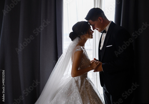 Side view of adorable couple in festival outfit, standing face to face in room, closing eyes, holding hands and feeling happy during wedding day