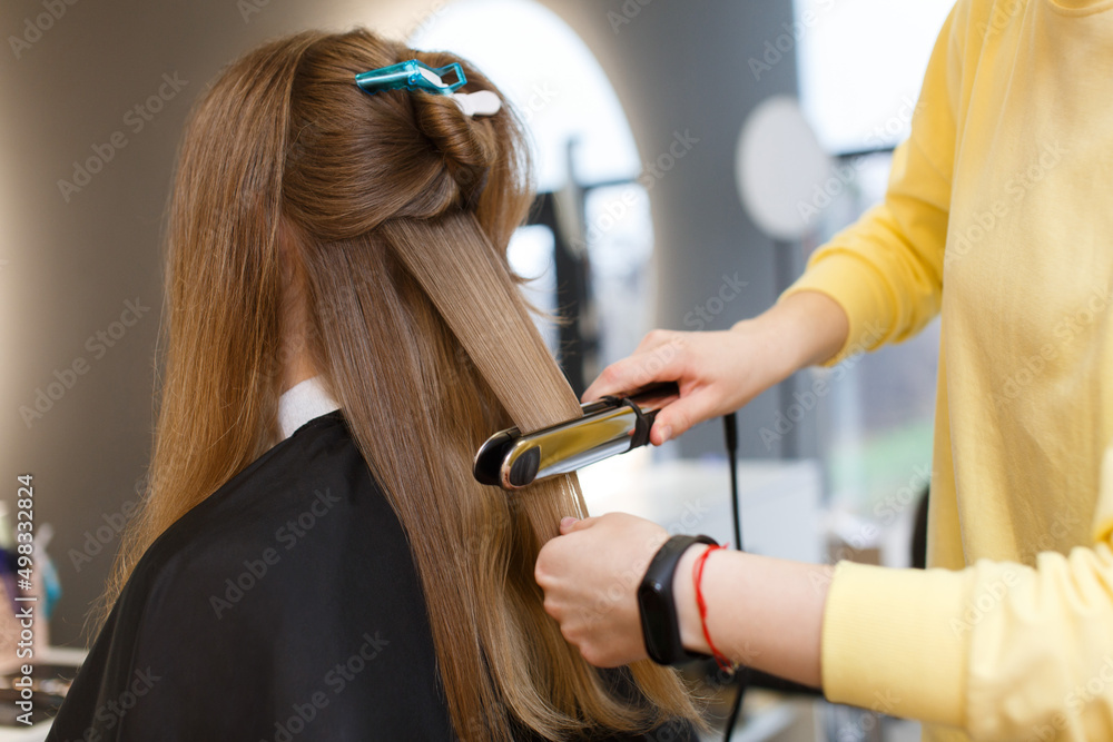 Naklejka premium hair straightening. Hairdressing services on background. process of haircuts . Hair styling process. hair master hands with professional curling iron close up portrait. Keratin recovery hair