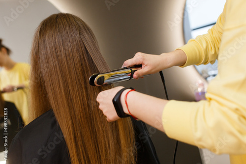 well groomed hair straightening. hair master hands in process of haircuts on background. Keratin recovery hair and protein treatment pile with professional ultrasonic iron tool. Concept straighten.