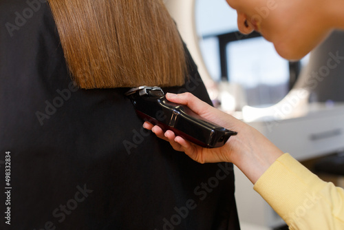 Smiling hairdresser doing hair cutting of woman using clipper in salon. hands of female hairdresser in process recovery haircut on background . Professional stylist cutting woman's hair, closeup