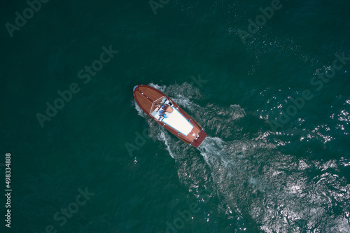 People on an Italian wooden boat, top view. Old boat on Lake, Italy. Classic wooden boat in motion drone view.