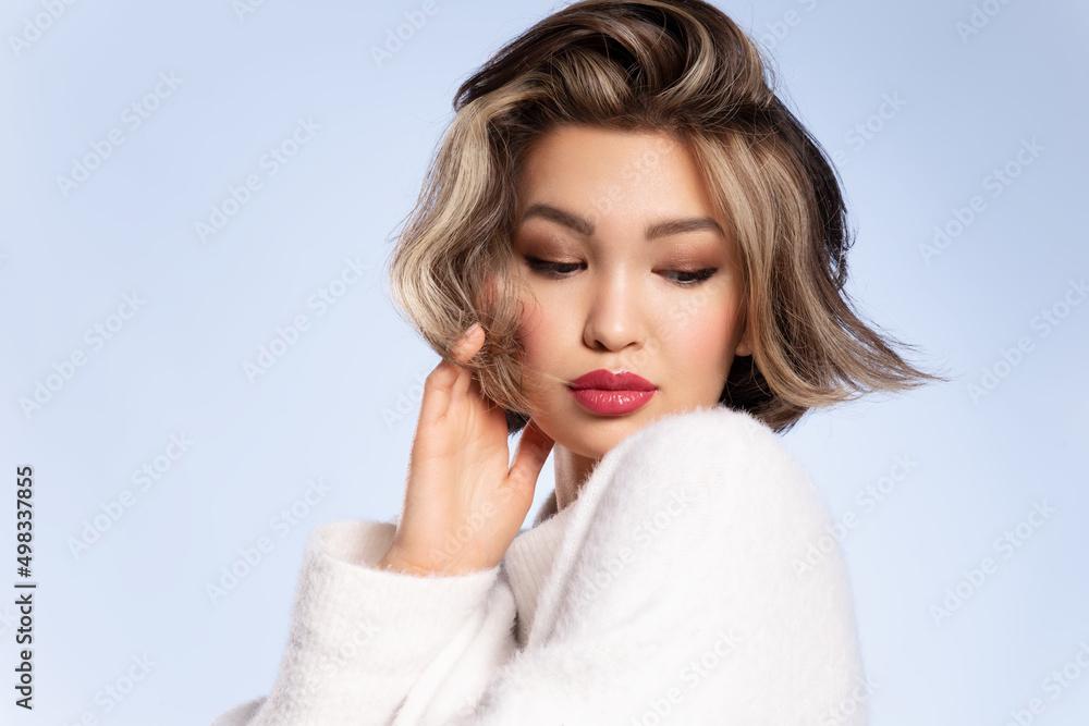 Pretty stylish young asian woman with stylish short haircut wearing cozy white sweater posing on blue studio background. Haircare, hairstyling cosmetics advertisement. Natural beauty. Pretty stylish young asian woman with stylish short haircut wearing cozy white sweater posing on blue studio background. Haircare, hairstyling cosmetics advertisement. Natural beauty.