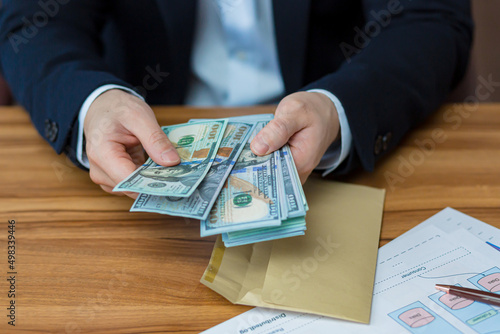 Close up photo hands of young businessman man holds and opens envelope with money, dollars, currency, holds in hands at table, shows, counts