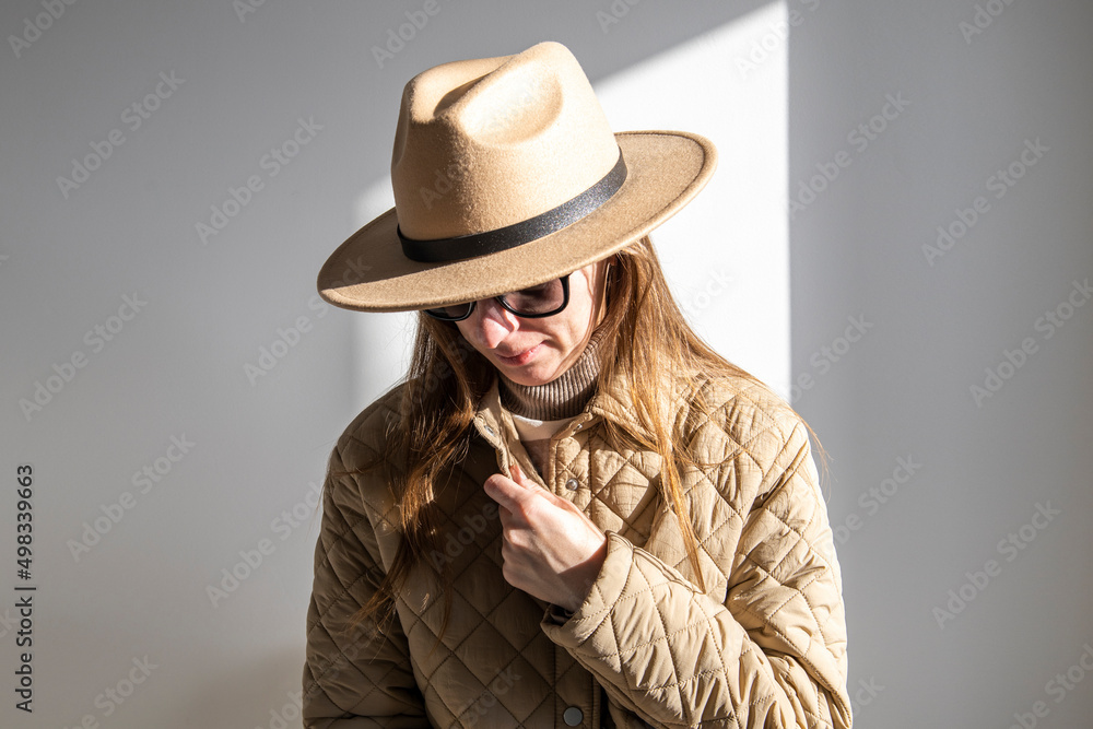 Young woman in a jacket in sunglasses in a hat against a white wall. Young woman in a jacket in sunglasses in a hat against a white wall.