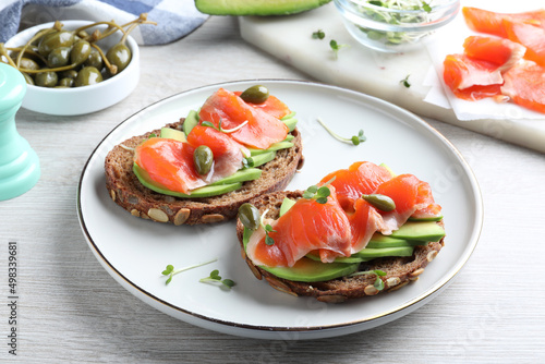 Delicious sandwiches with salmon, avocado and capers on white wooden table