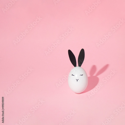 Canvas Print White easter egg with bunny face and eyes on bright pink background with shadow