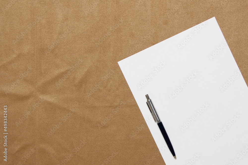Template of white paper with pen lies diagonally on light brown cloth background. Concept of business plan and strategy. Stock photo with empty space for text and design. Template of white paper with pen lies diagonally on light brown cloth background. Concept of business plan and strategy. Stock photo with empty space for text and design.