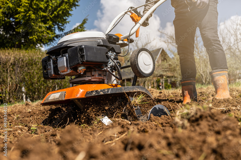 Fototapeta premium Close up photo of gardener cultivate ground soil rototiller , tiller tractor, cutivator, miiling machine, prepare for planting crop, spring. modern farming, technology agriculture.