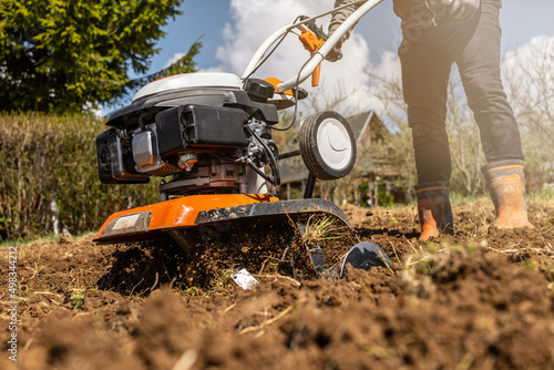 Close up photo of gardener cultivate ground soil rototiller , tiller tractor, cutivator, miiling machine, prepare for planting crop, spring. modern farming, technology agriculture. photo