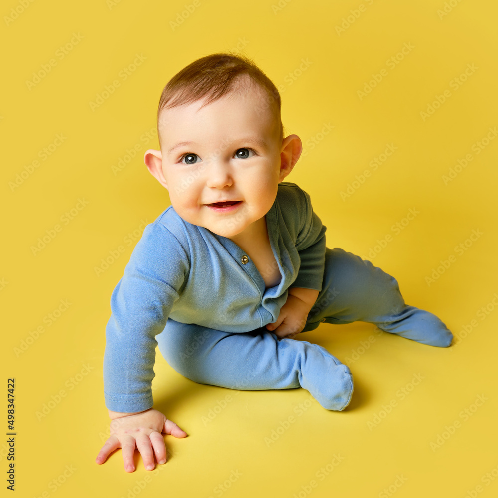 Happy toddler baby sits on studio yellow background. Funny child boy at the age of six months with a smile on his face, copy space Happy toddler baby sits on studio yellow background. Funny child boy at the age of six months with a smile on his face, copy space