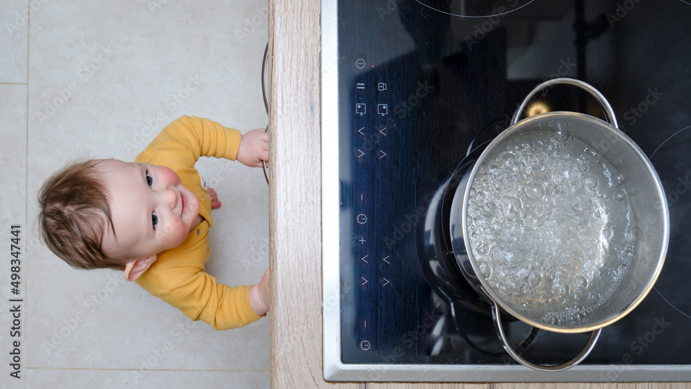 Toddler baby boy looks at a pot of boiling water. Child safety issues