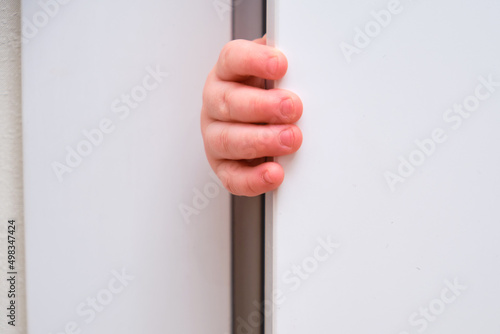 Toddler baby boy holds the edge of the open door with his hand. Close-up child hand at the door jamb photo