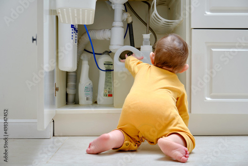 Bild auf Leinwand Toddler baby boy is playing with detergents and cleaning products in an open kitchen cabinet