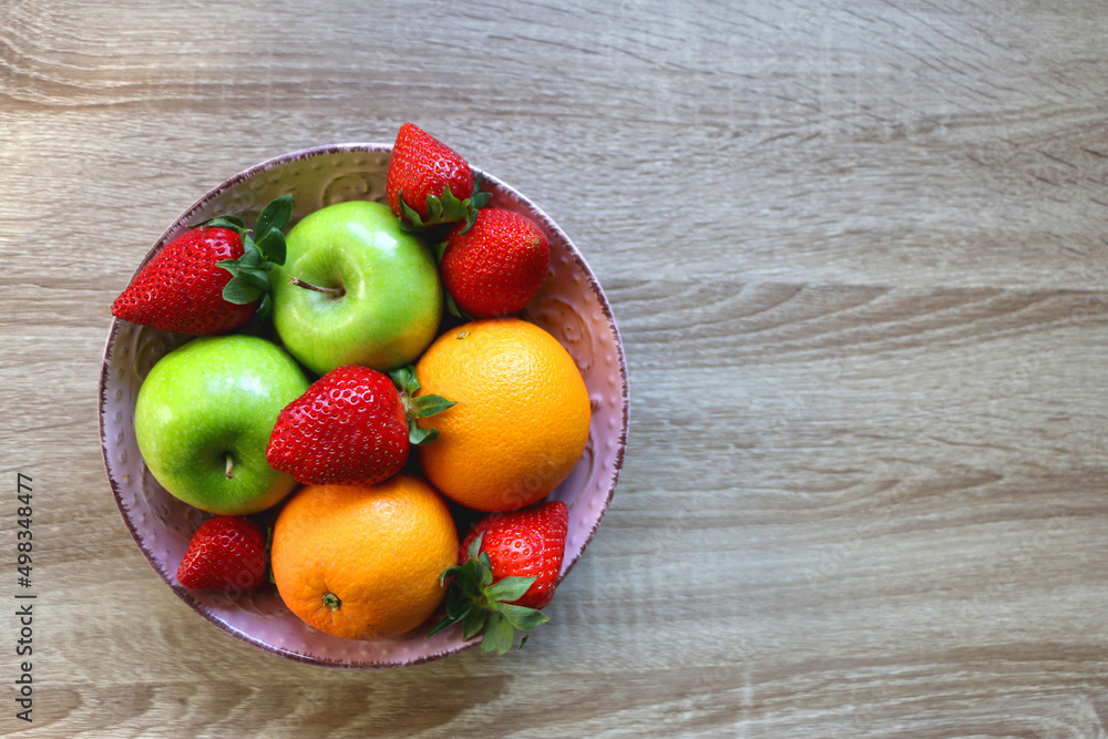 Naklejka Pink bowl filled with fresh apples, oranges and strawberries on wooden table. Flat lay.