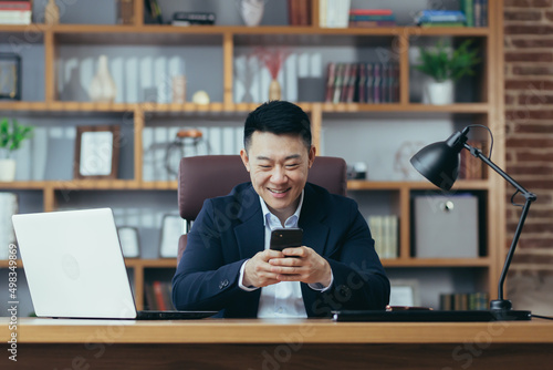 Young handsome happy asian businessman man rejoices, got good news, uses phone. Concluded an agreement, received a contract
