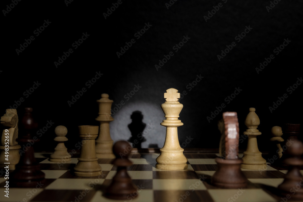 Chess king under spotlight. Studio shot of chess pieces on a chessboard illuminated by a stage light. Low-key. Chess king under spotlight. Studio shot of chess pieces on a chessboard illuminated by a stage light. Low-key.