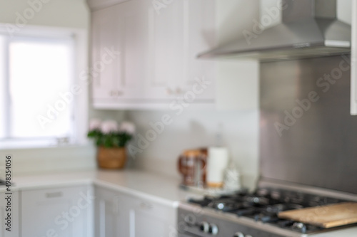 Blurred photo of modern new kitchen with light grey furniture and quartz worktop, light interior trendy units. Granite sink under big window