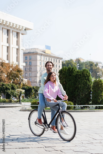 Happy man riding bicycle with girlfriend on urban street at daytime.