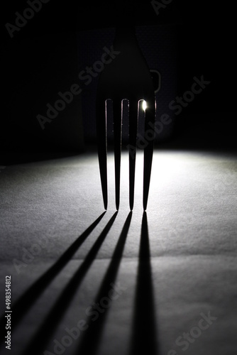 Tenedor para manipular comidas en contraluz entre sus dientes forma una figura en sombra reflejada sobre el piso, presenta un hermoso diseño abstracto con fondo negro photo