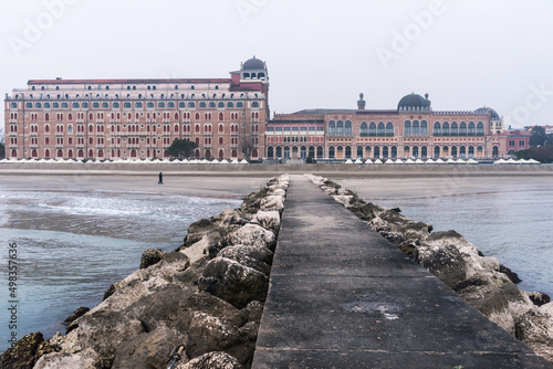 Steg mit Steinen im Meer am Lido di Venezia bei Nebel, Blick auf nostalgisches Gebäude im Jugendstil photo