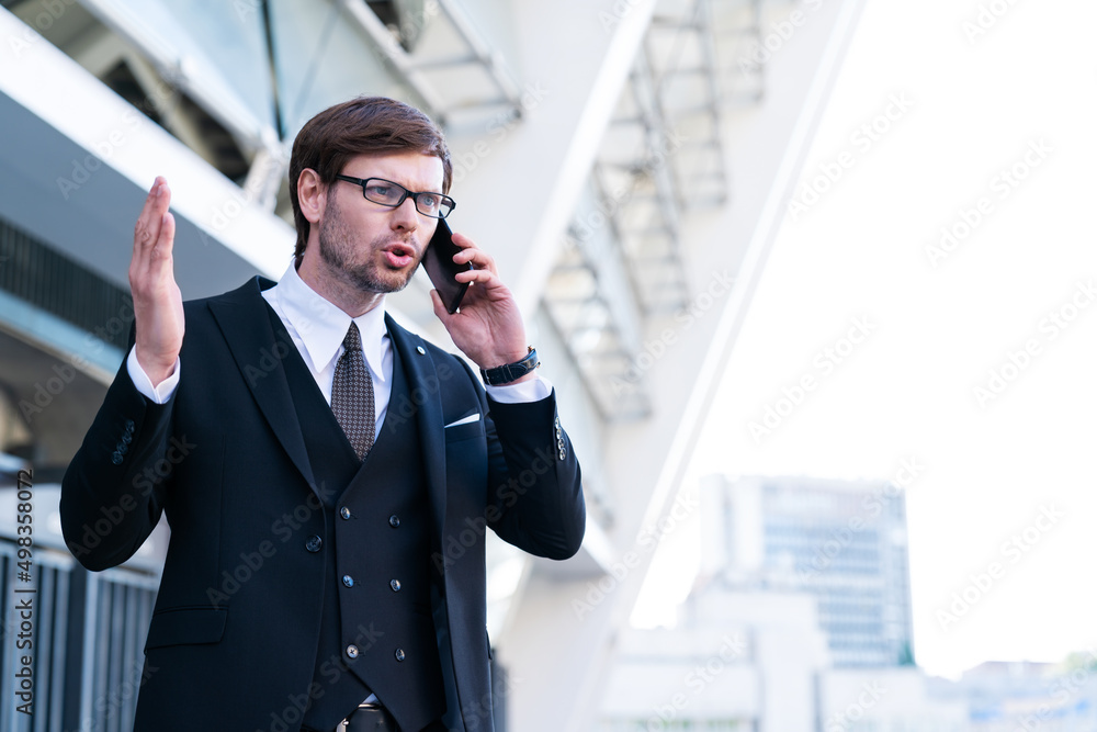 Portrait of stressed businessman speaks by phone wave his hand in frustration. Overworked angry manger entrepreneur in big city business district. Upset man in suit with office building in background. Portrait of stressed businessman speaks by phone wave his hand in frustration. Overworked angry manger entrepreneur in big city business district. Upset man in suit with office building in background.