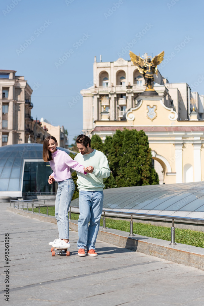 Cheerful woman riding penny board with boyfriend on urban street.
