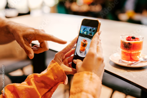 Close up shot of a female hand holding smartphone to take a photo of smoothie during a date with a handsome young man in a cafe. Selective focus on smartphone display.