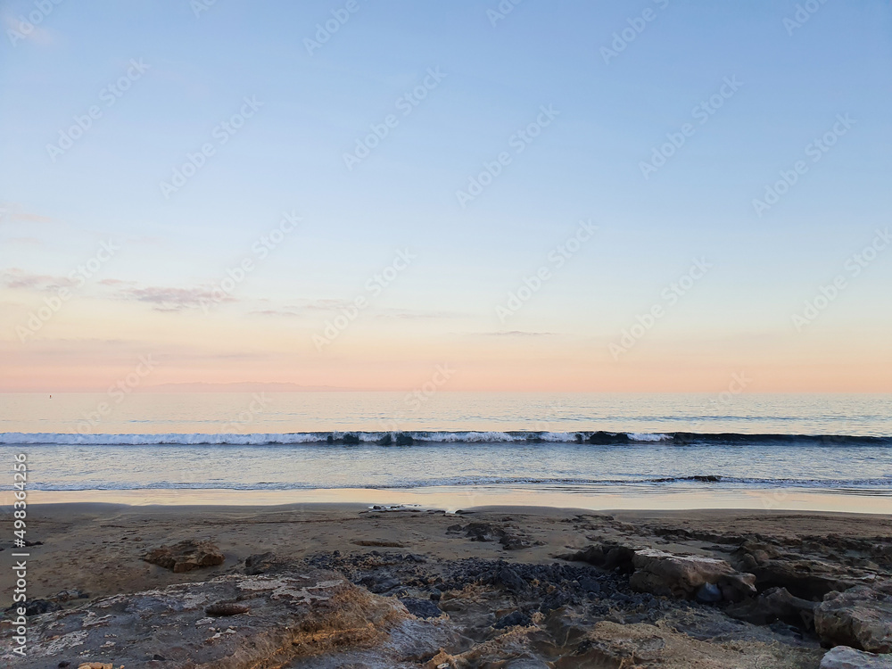 Horizontal photo of a soft pink sunset with a long small wave
