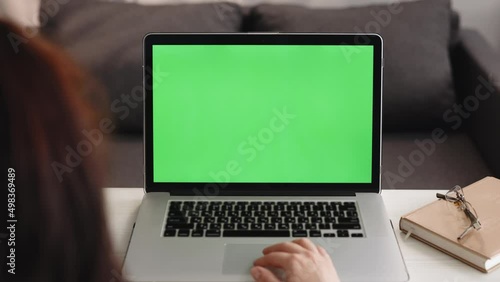 Over the shoulder shot of caucasian woman looking at green screen chroma key. Office person using laptop computer with laptop green mockup screen. photo