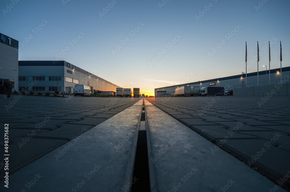 Logistics area with halls and trucks at sunset. Transport and storage of goods.