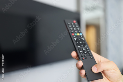 Black remote control in hand in front of TV
