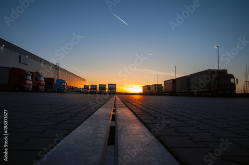 Logistics area with halls and trucks at sunset. Transport and storage of goods.