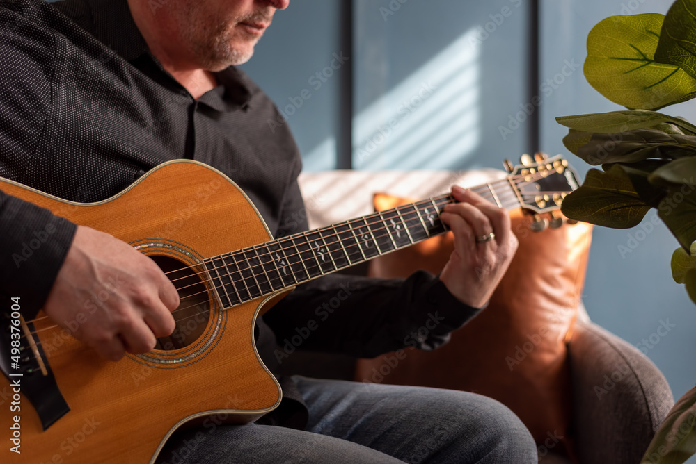 Obraz premium Man playing acoustic guitar at home in natural light