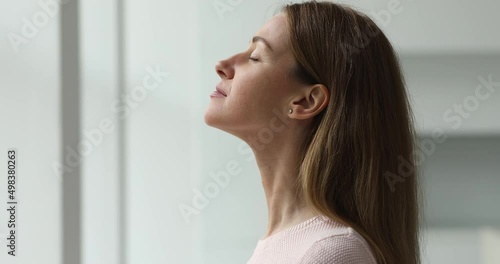 Calm young woman taking deep breath of fresh air meditating with eyes closed standing indoor, close up side profile view. Enjoy moment of peace, do mental relaxation exercises, feels no stress concept photo