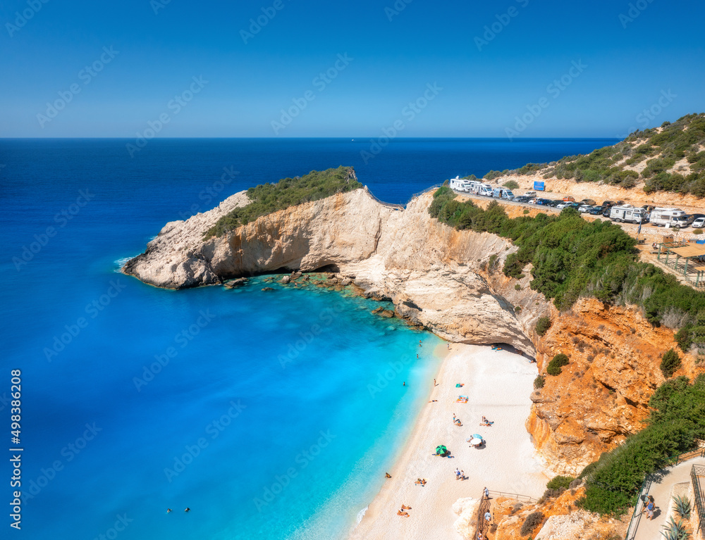 Aerial view of blue sea, rock, sandy beach with umbrellas at sunny day in summer. Porto Katsiki, Lefkada island, Greece. Beautiful landscape with sea coast, swimming people, azure water. Top view