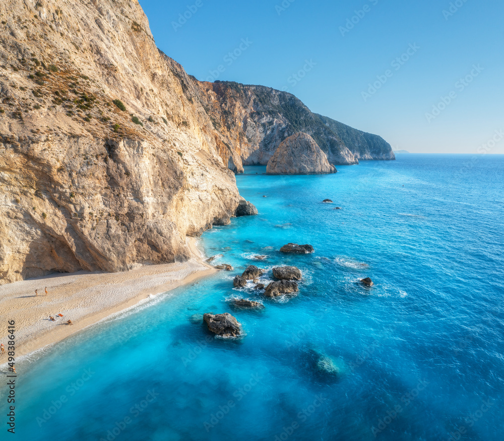 Aerial view of blue sea, rocks, sandy beach with people at sunny day in summer. Porto Katsiki, Lefkada island, Greece. Beautiful landscape with sea coast, stones in azure water, waves, sky. Top view Aerial view of blue sea, rocks, sandy beach with people at sunny day in summer. Porto Katsiki, Lefkada island, Greece. Beautiful landscape with sea coast, stones in azure water, waves, sky. Top view