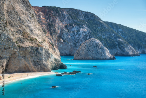 Aerial view of blue sea, rocks, sandy beach with people at sunny day in summer. Porto Katsiki, Lefkada island, Greece. Beautiful landscape with sea coast, stones in azure water, waves, sky. Top view