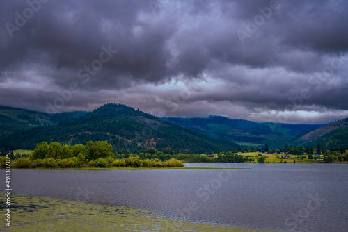 2022-04-11 COUER D'ALENE RIVER WITH A TREE LINED SHORE, MOUNTAINS AND A CLOUDY SKY photo