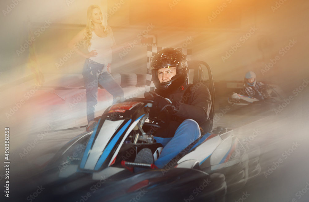 Diligent efficient positive man in helmet driving car for karting in sport club, woman with flag on background