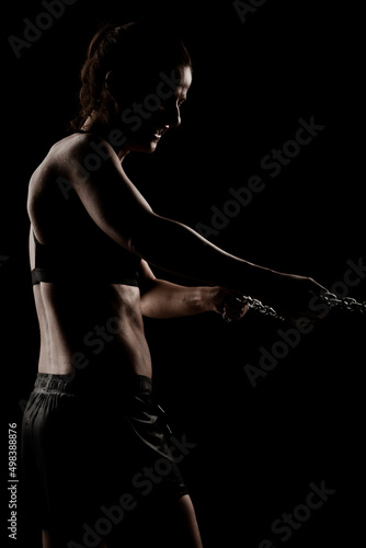 Strong fit girl with metal chain. Pulling and posing against black background..