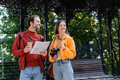 Cheerful travelers with coffee, binoculars and map looking away on urban street. © LIGHTFIELD STUDIOS