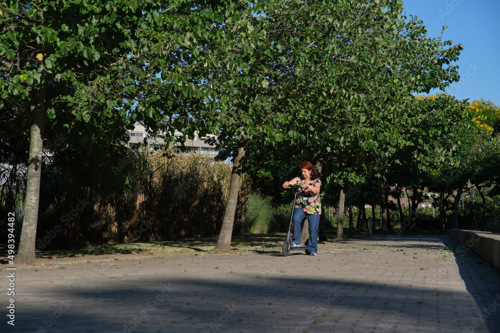 Latin mature woman practicing on her electric kick scooter, modern transport Latin mature woman practicing on her electric kick scooter, modern transport