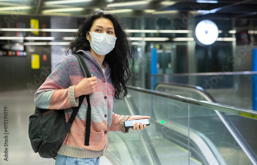 Asian woman in face mask with backpack walking in subway beside escolator