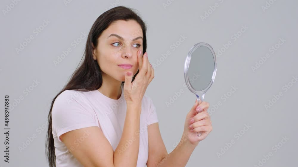Beautiful adult woman with perfect skin and smile holding a mirror she looking at her face on white background concept of skincare treatment cosmetics Beautiful adult woman with perfect skin and smile holding a mirror she looking at her face on white background concept of skincare treatment cosmetics