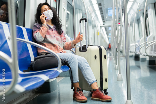 Portrait of young adult woman in protective face mask commuting in city using tube and talking on smartphone © JackF