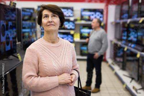 Portrait of a thoughtful European woman standing in the department with televisions in an electronics store